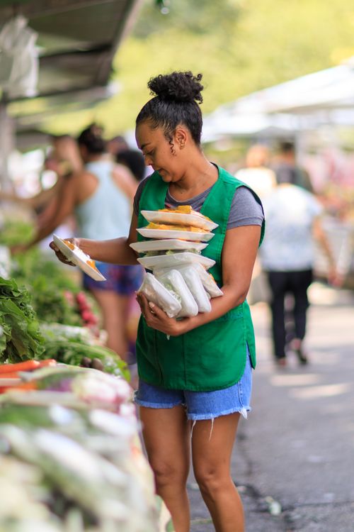 Free A woman in a green vest arranging vegetables at an outdoor market, showcasing fresh produce. Stock Photo