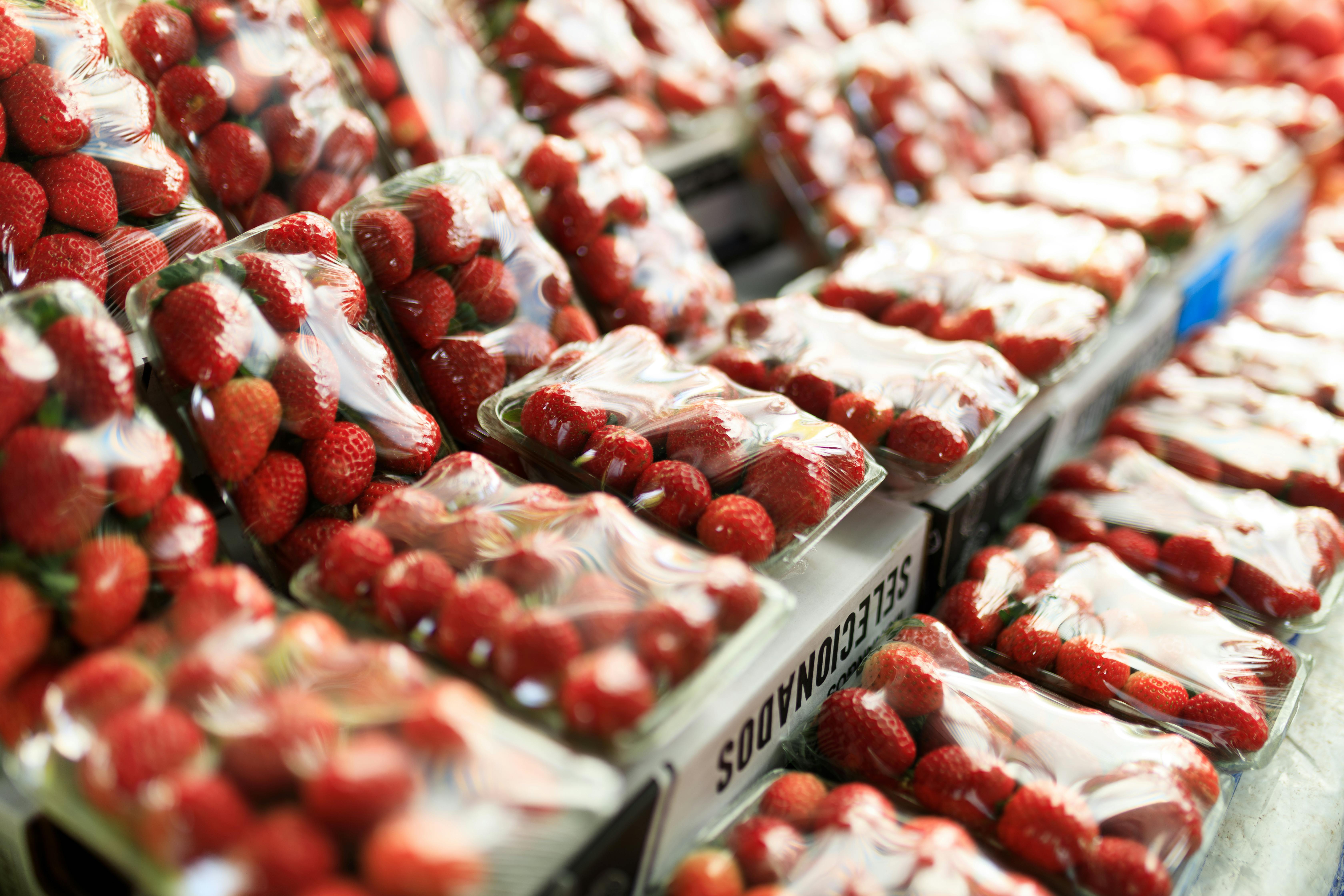 Rows of fresh strawberries in transparent packaging displayed at a market stand.