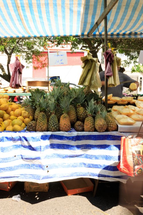 Free Vibrant market stall with pineapples, mangoes, and bread under a striped canopy. Stock Photo