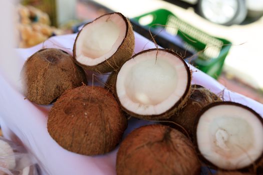 Close-up of fresh coconuts split open and displayed on a white surface in an outdoor market setting.