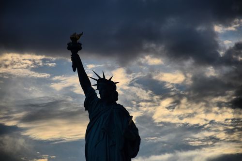 Free Dramatic silhouette of the Statue of Liberty against a cloudy evening sky in New York City. Stock Photo