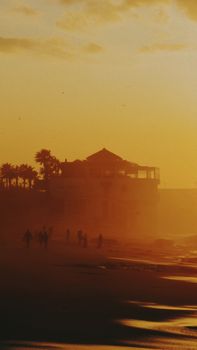 Silhouetted people and palm trees against the golden sunset at Rabat beach.
