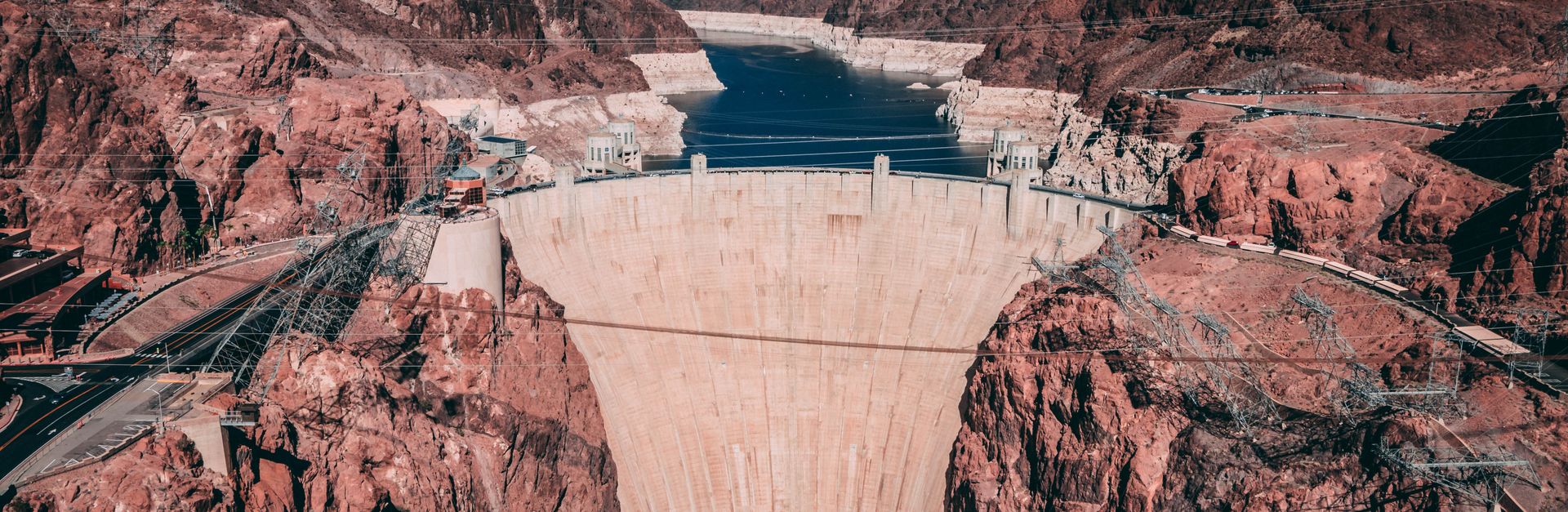 Explore breathtaking aerial view of Hoover Dam surrounded by rugged red rocks and blue sky.
