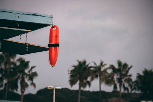 Orange lifeguard buoy hanging from a beach structure with palm trees in the background at sunset.