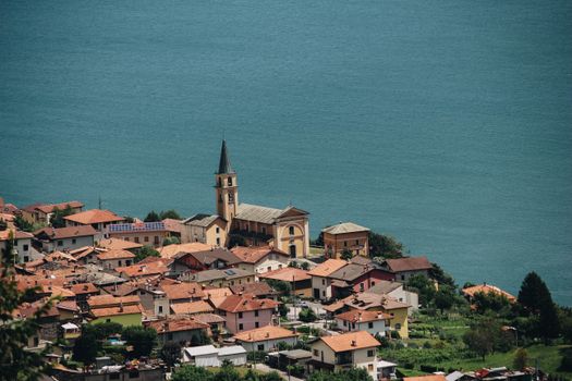 Charming Italian village with church and red roofs by a tranquil blue lake.