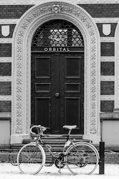 Black and white photo of bicycle parked by a vintage ornate door in Malmö, Sweden.