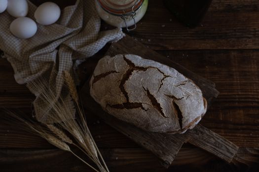 Artistic shot of homemade rustic bread with eggs and wheat on wooden table.