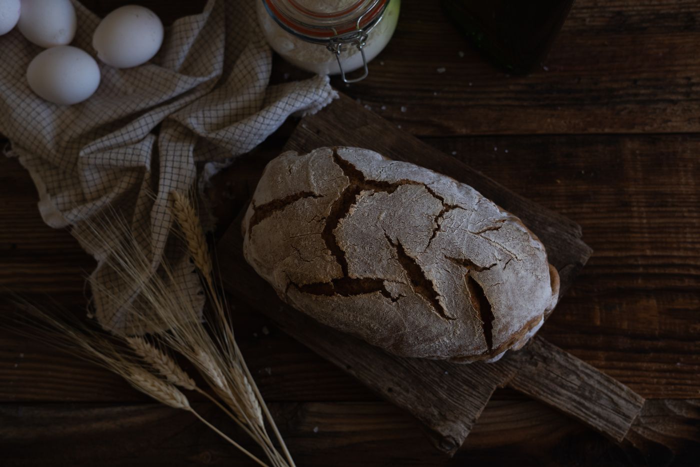 A rustic homemade loaf with eggs and wheat on a wooden table — photo by hello aesthe on Pexels