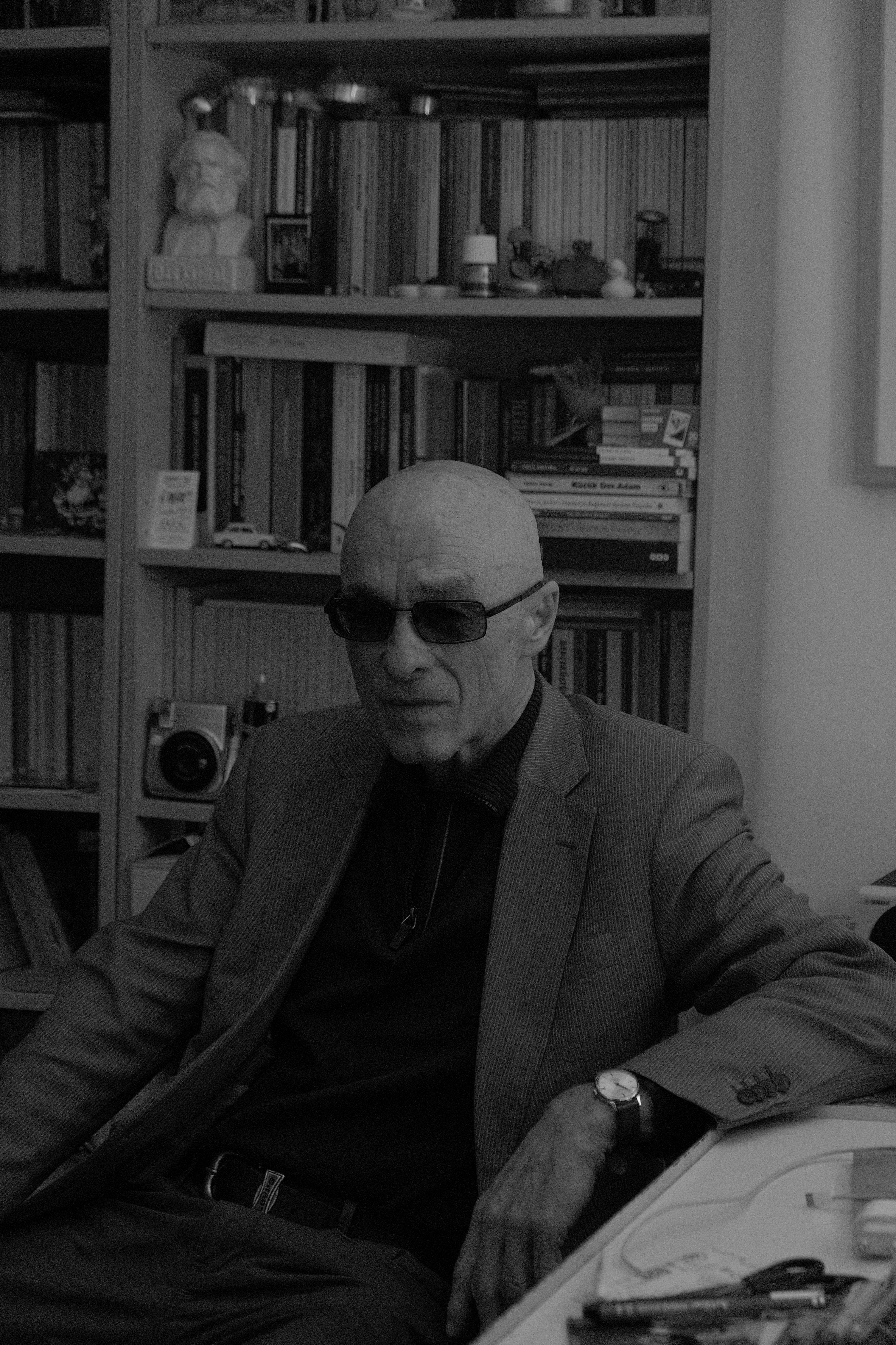 Stylish black and white portrait of a man sitting indoors with bookshelves.
