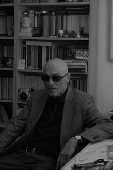 Stylish black and white portrait of a man sitting indoors with bookshelves.