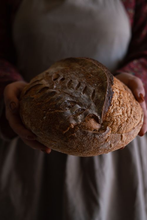 Free Close-up of artisan bread held by a baker in a dimly lit setting, showcasing rustic craftsmanship. Stock Photo