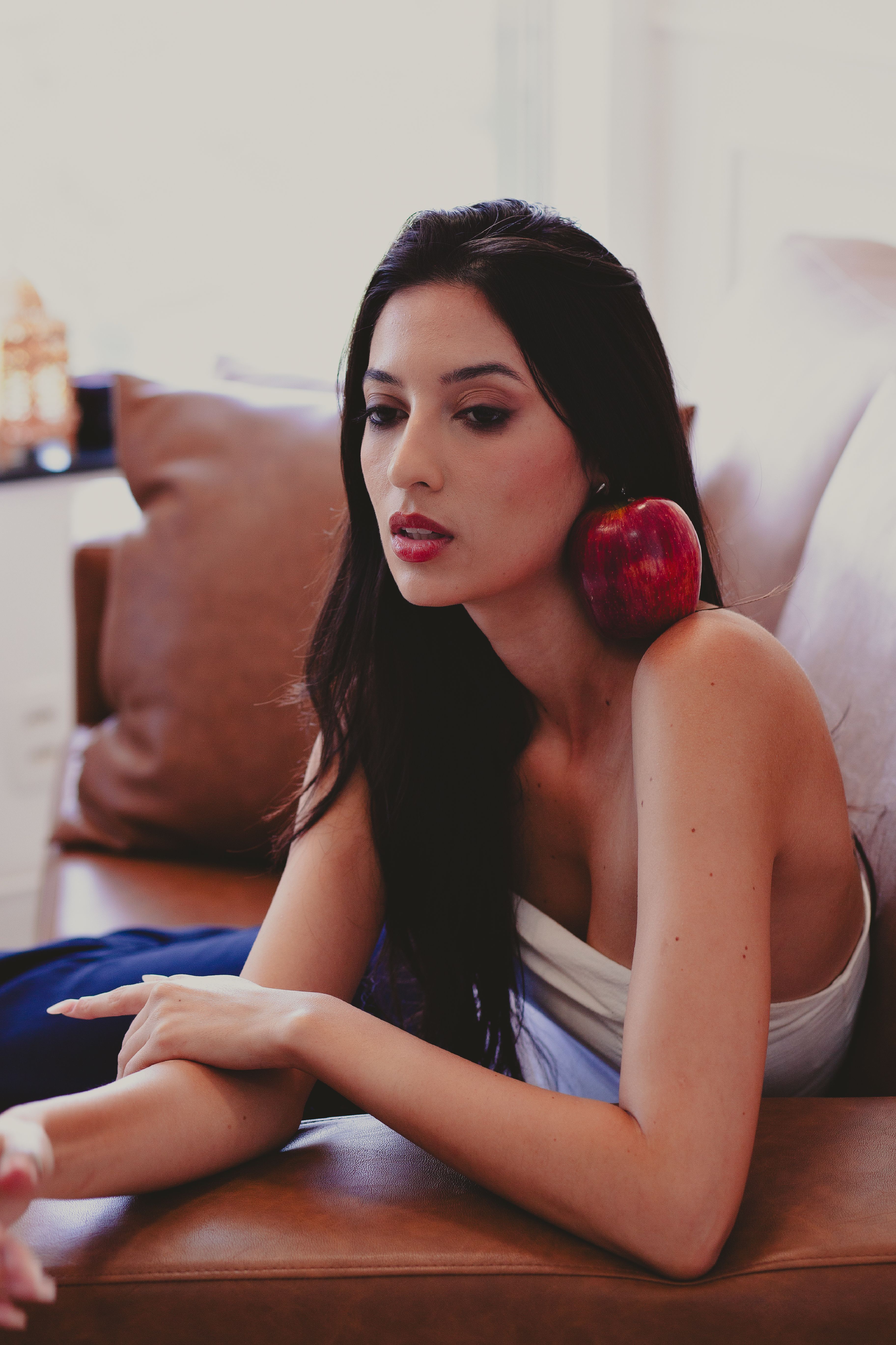 Stylish woman indoors with a red apple on shoulder, conveying elegance and modernity.