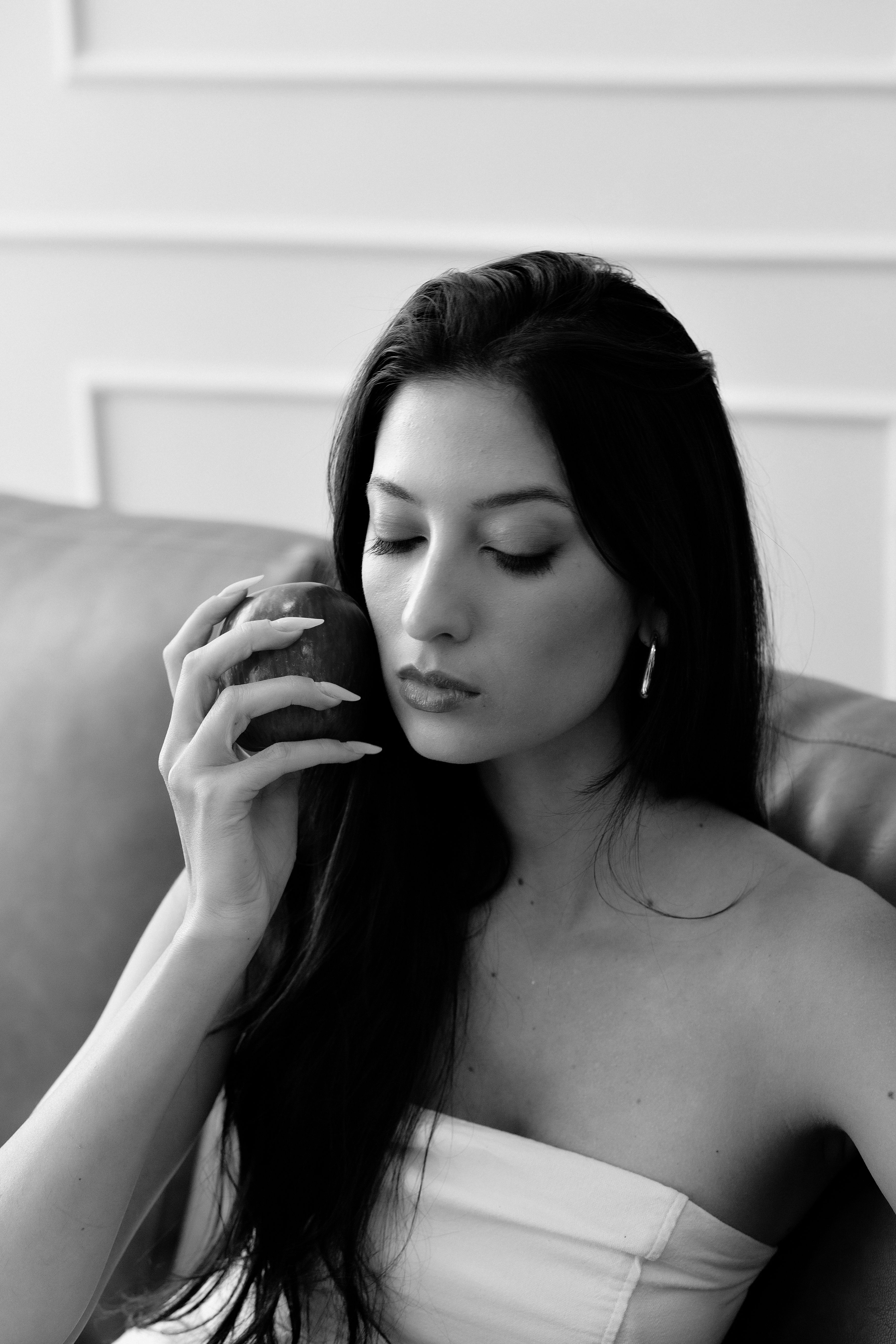 Portrait of a woman holding an apple, sitting indoors in black and white.