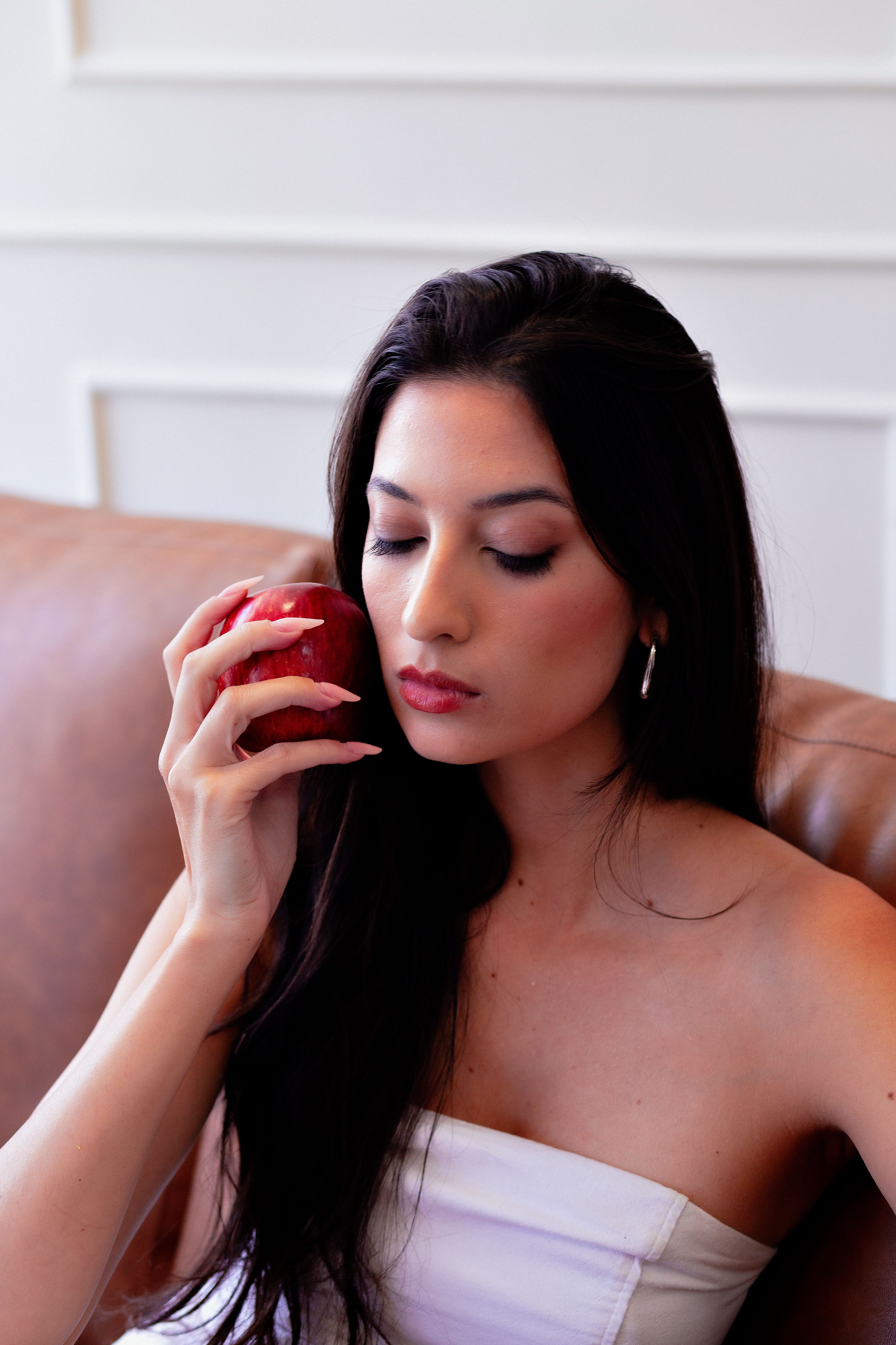 Serene woman holding an apple in a modern indoor setting, embodying sophistication and calm.