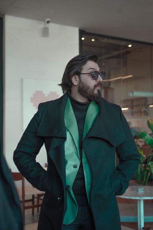 Free Fashionable man in a green coat poses confidently indoors. Stock Photo