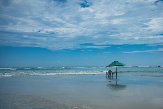 Calm beach view at Pipa, Brazil with a single umbrella and chairs, under a bright, cloudy sky.