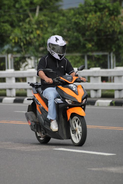 Free A person in helmet riding an orange scooter on a city street. Stock Photo