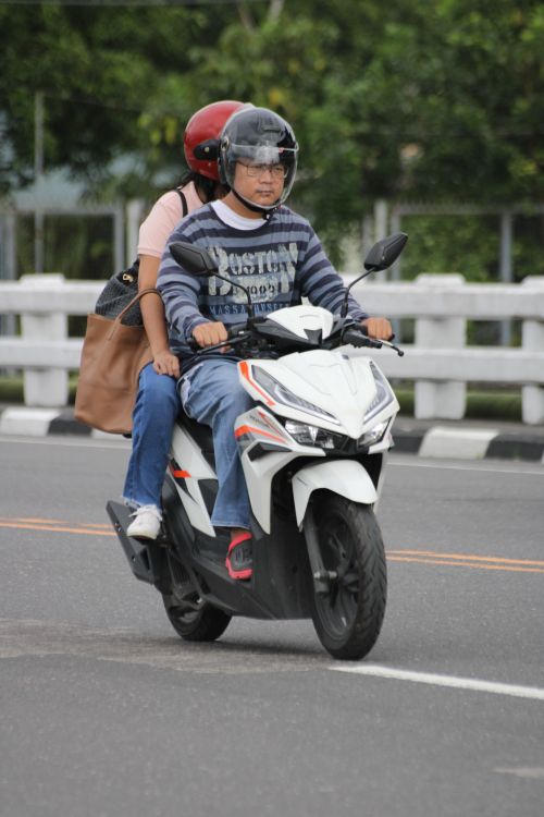 Free Two adults riding a white scooter on a city street wearing helmets. Stock Photo