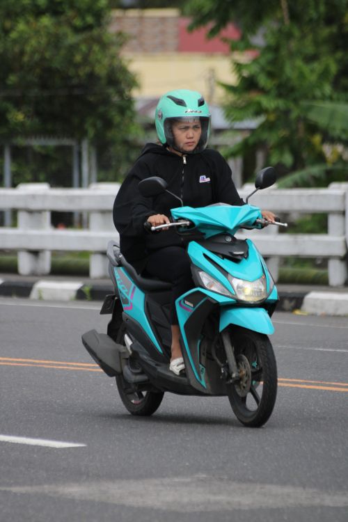 Free A woman in a black jacket rides a turquoise scooter on a city street. Stock Photo