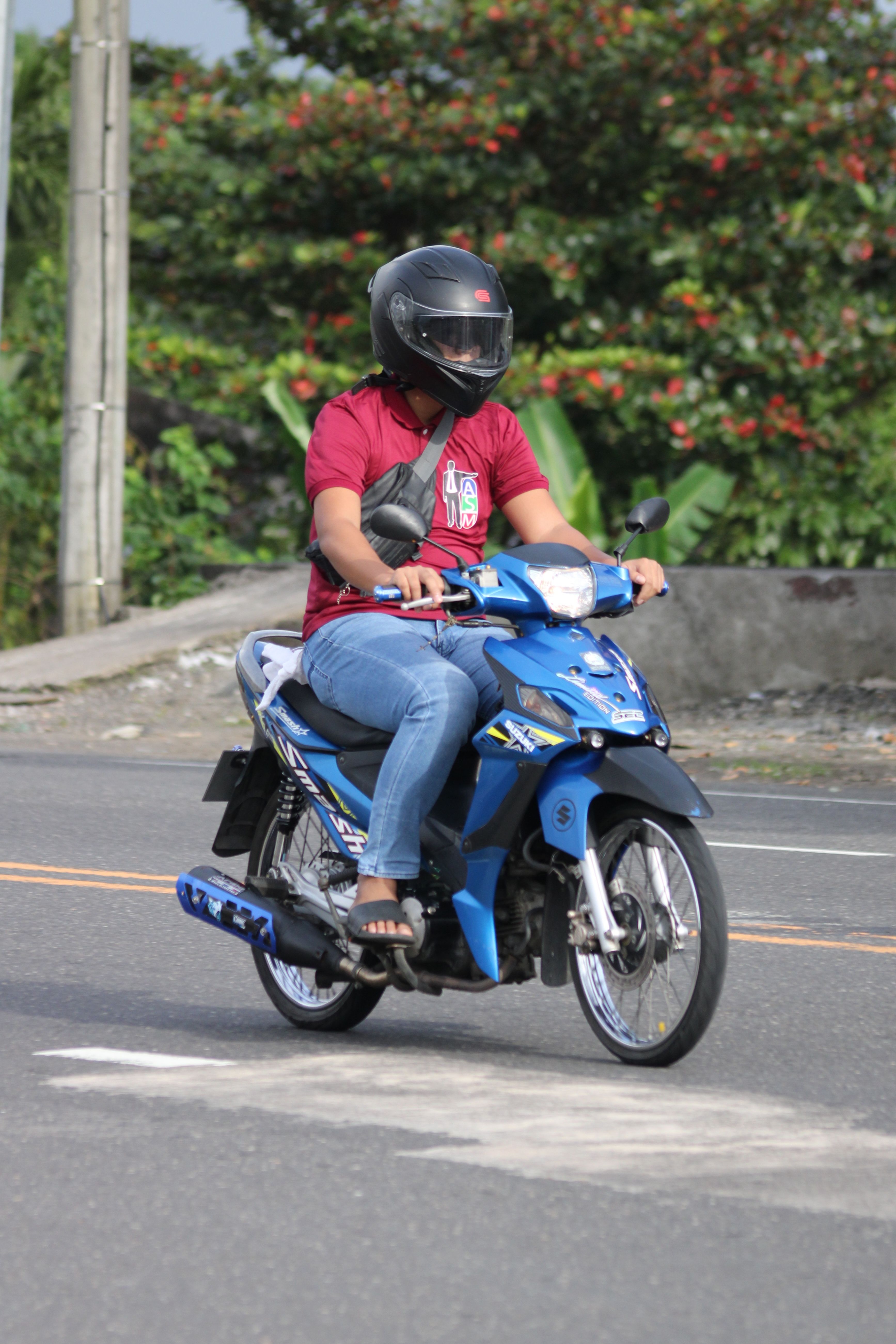 A person rides a blue motorcycle on a city street during the day.