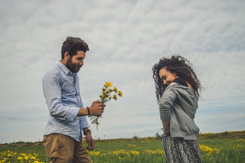 Man in Blue Long Sleeve Shirt Giving A Woman A Bunch of Yellow Flowers