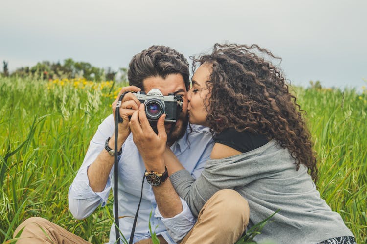 Woman Kissing A Man Holding A Camera