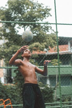 A young soccer player practices heading skills at an outdoor field.