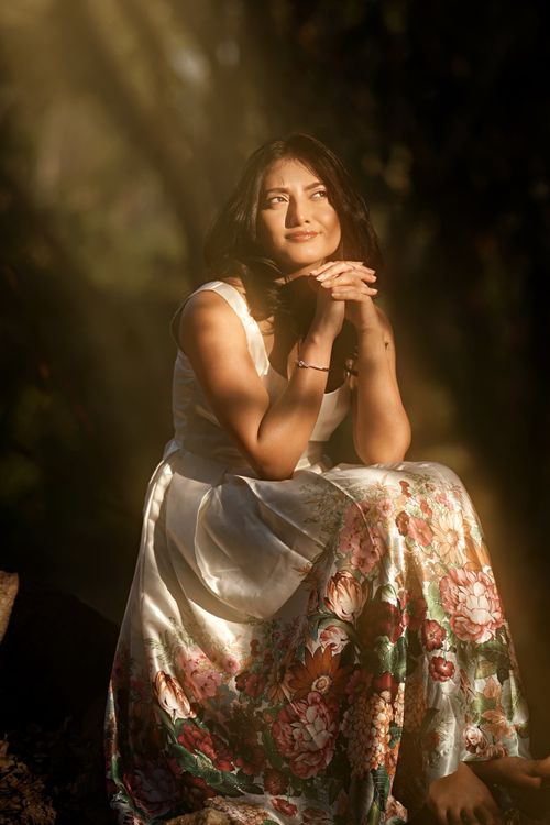 Free A woman in a floral dress sits peacefully in a sunlit natural setting, exuding tranquility. Stock Photo
