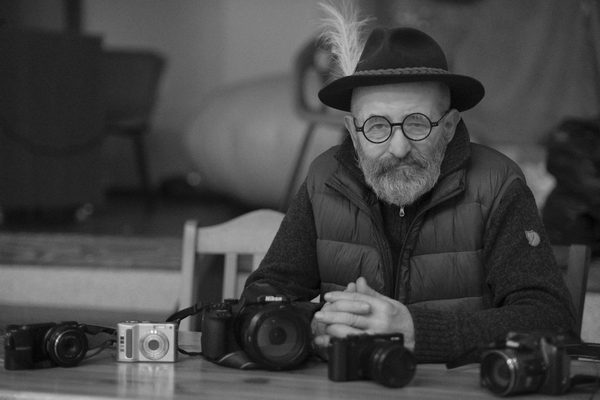 Black and white portrait of an elderly man with a collection of vintage cameras.