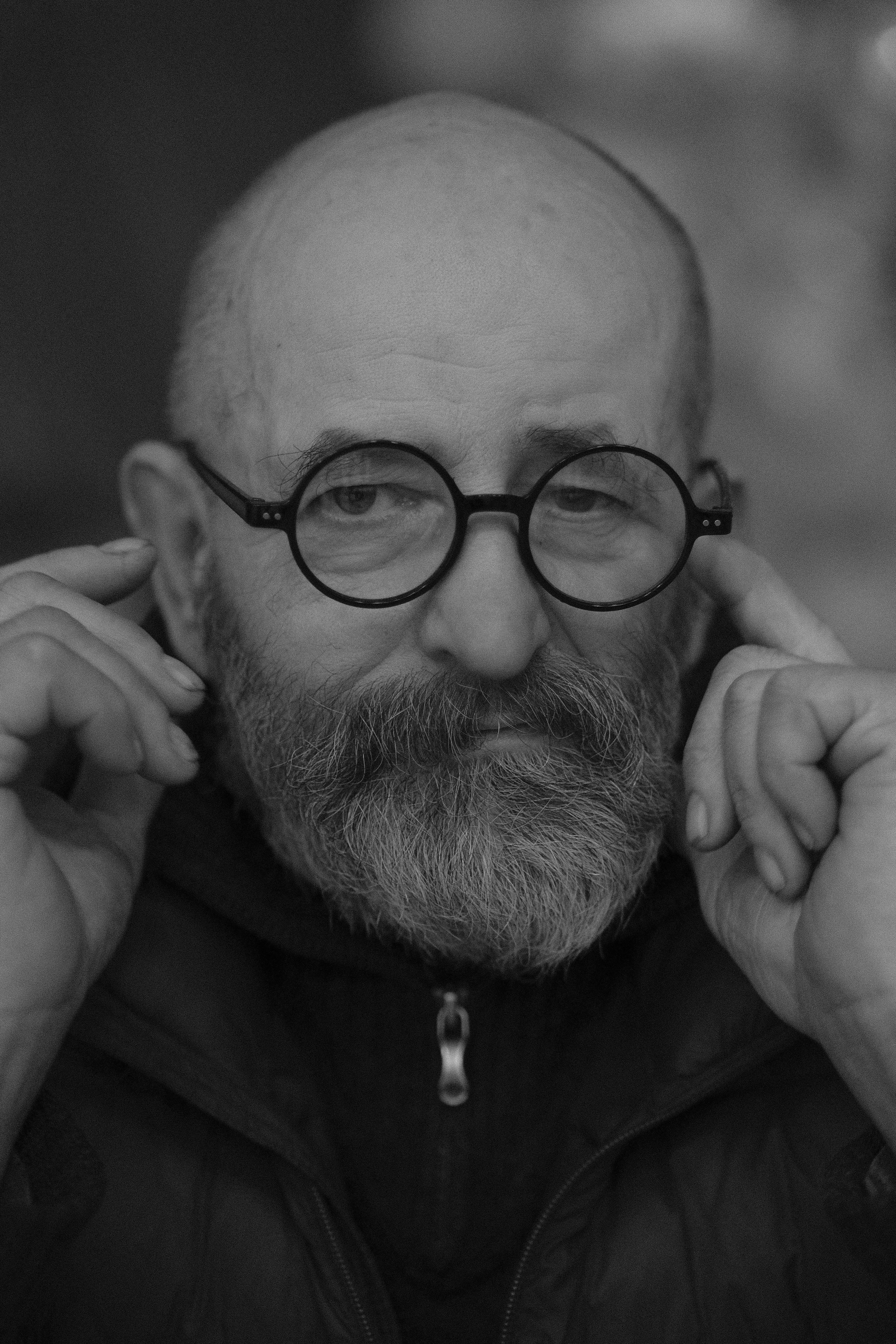 Artistic black and white portrait of a bearded man adjusting his round glasses.