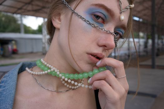 Close-up portrait of a woman with vibrant makeup and layered necklaces, showcasing creative jewelry artistry.