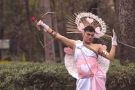 Person in a Cupid costume posing artistically with bow in a park.