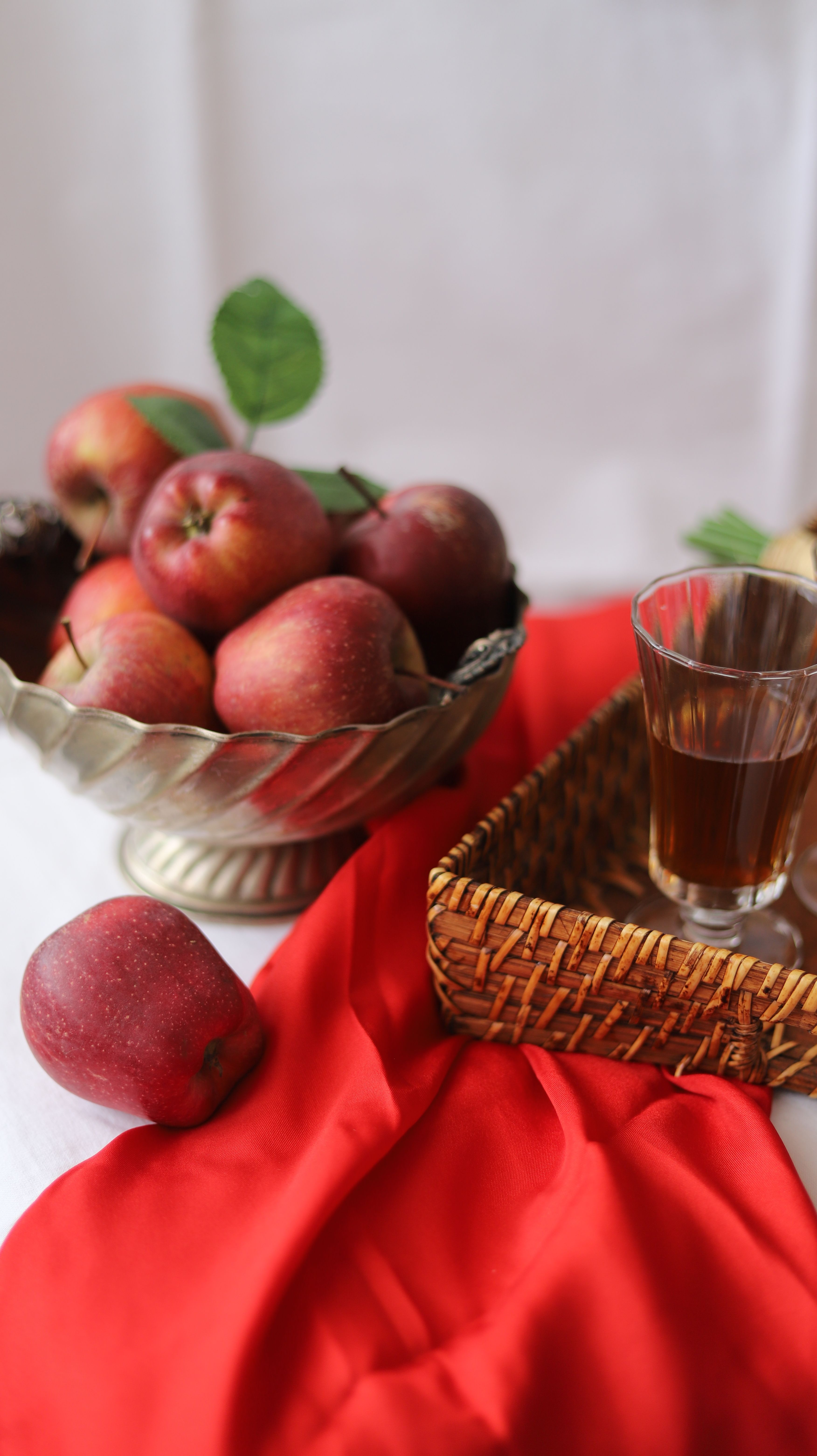 A basket of red apples with a glass of apple juice on a vibrant red cloth.