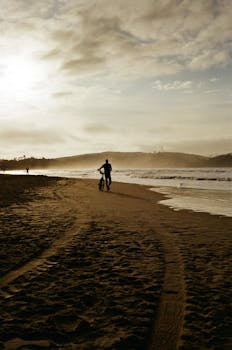 Silhouette of a cyclist on a beach at sunrise in Armação dos Búzios, Brazil.