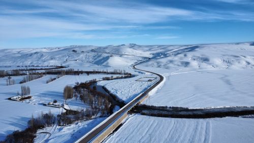 Free Aerial shot of a snowy landscape featuring a winding road and vast white fields under a bright blue sky. Stock Photo