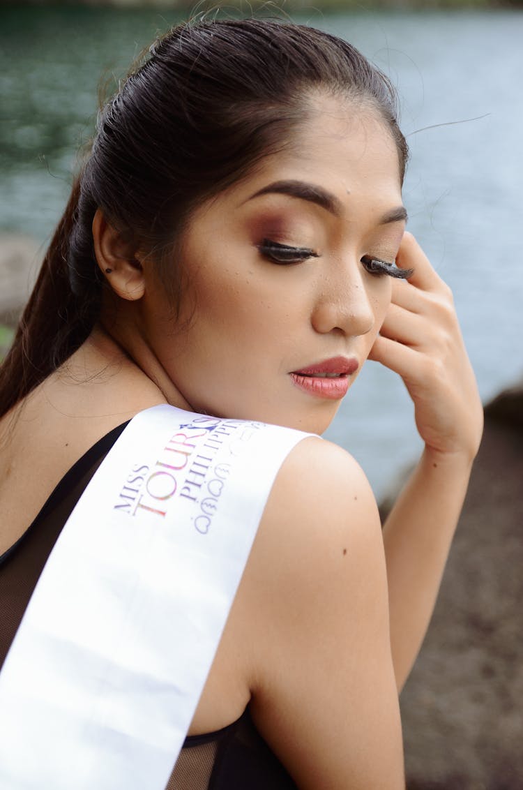 Woman Wearing White Sash With Left Hand On Face