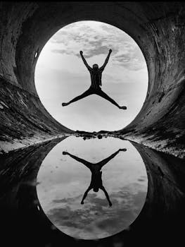 Black and white silhouette of a person jumping with a reflection in a tunnel.