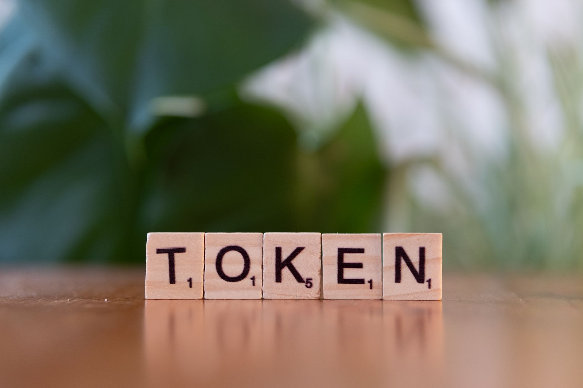 Close-up of Scrabble tiles spelling 'Token' on a wooden surface with a blurred green background.