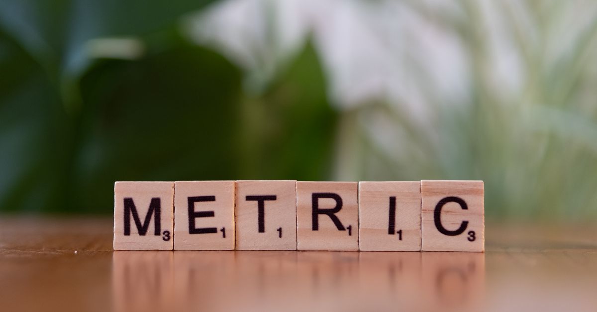 Close-up of wooden tiles spelling 'Metric' on a table, with a blurred green background.