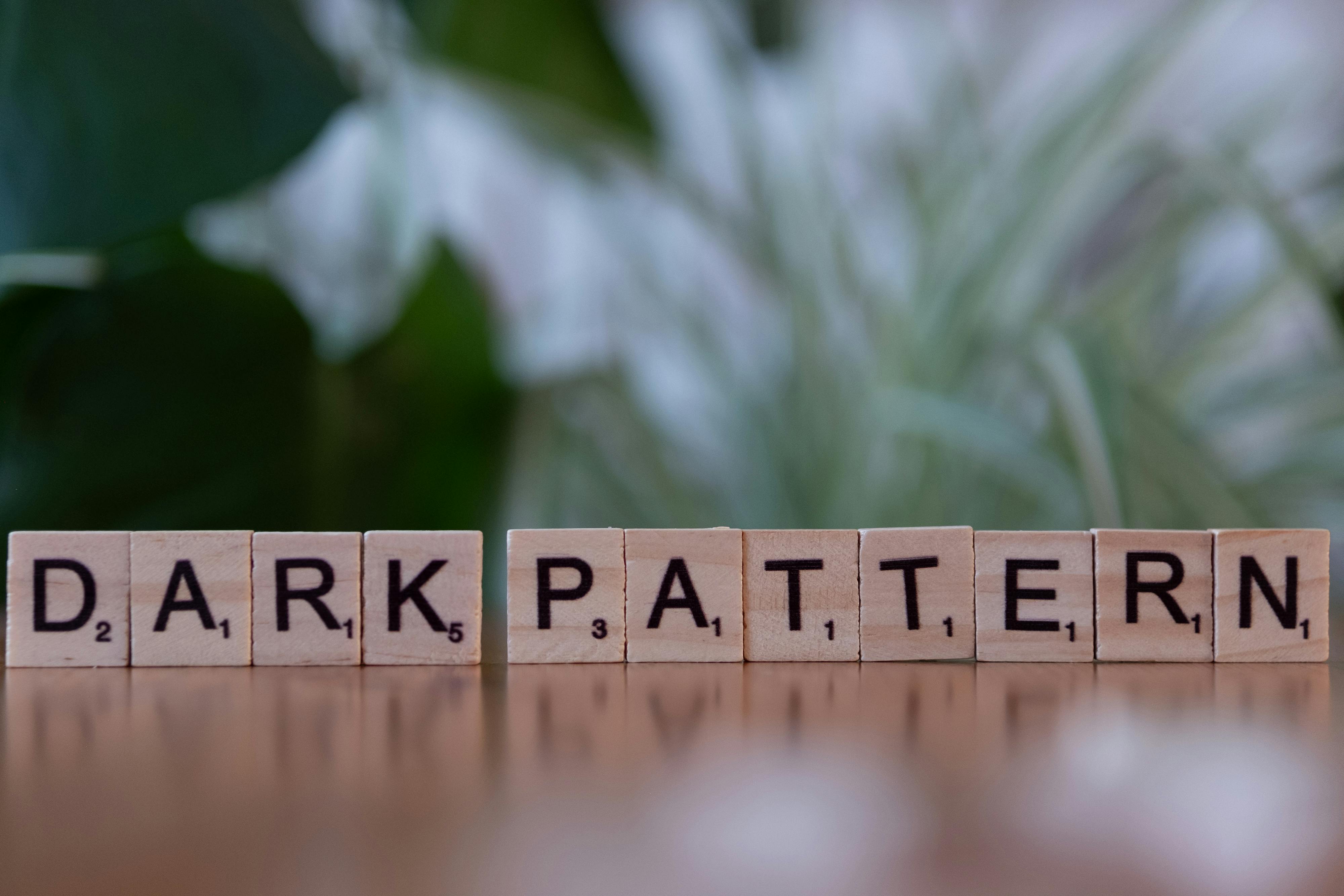 Wooden tiles spelling 'dark pattern' highlighting deceptive design in UX.