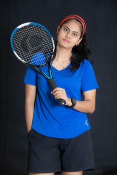 Young woman in sports attire holding a tennis racket in an indoor studio setting.
