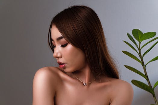 Close-up of a woman looking down, wearing an elegant necklace, alongside a green plant.