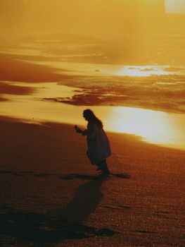 A woman walks along a beach in Rabat, Morocco, with a vibrant sunset reflecting on the water.