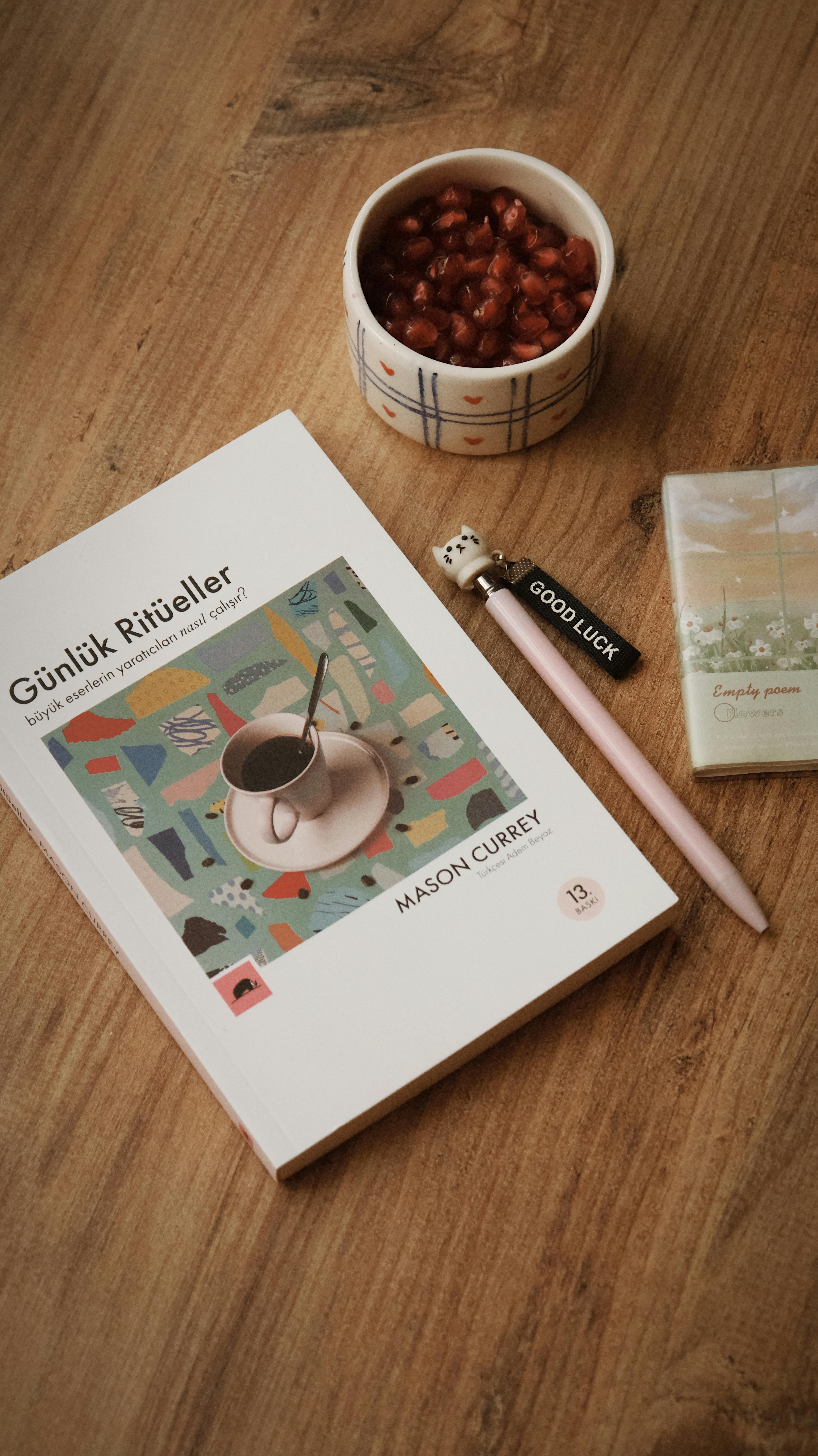 Flat lay of a book, snack cup with pomegranate seeds, pencil, and eraser on a wooden surface.
