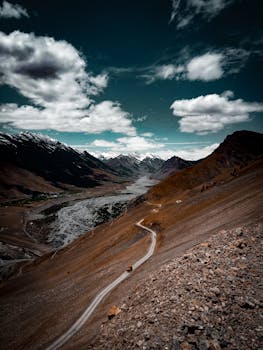 在动态的天空下，蜿蜒的道路穿过崎岖的山区地形，展现出戏剧性的视图