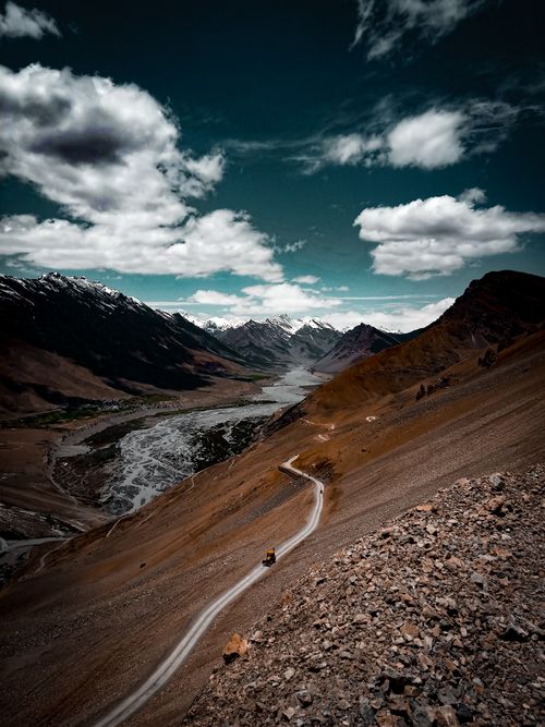 Free Dramatic view of a winding road through rugged mountain terrain under a dynamic sky. Stock Photo