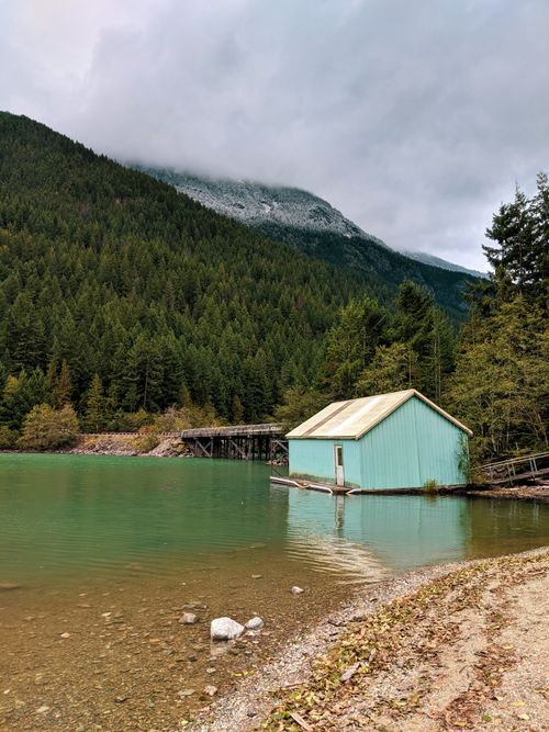 Free Scenic view of a quaint lake house by a serene mountain lake surrounded by pine forests. Stock Photo