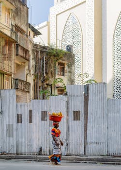 A woman in traditional attire balances a basket in a vibrant urban scene.