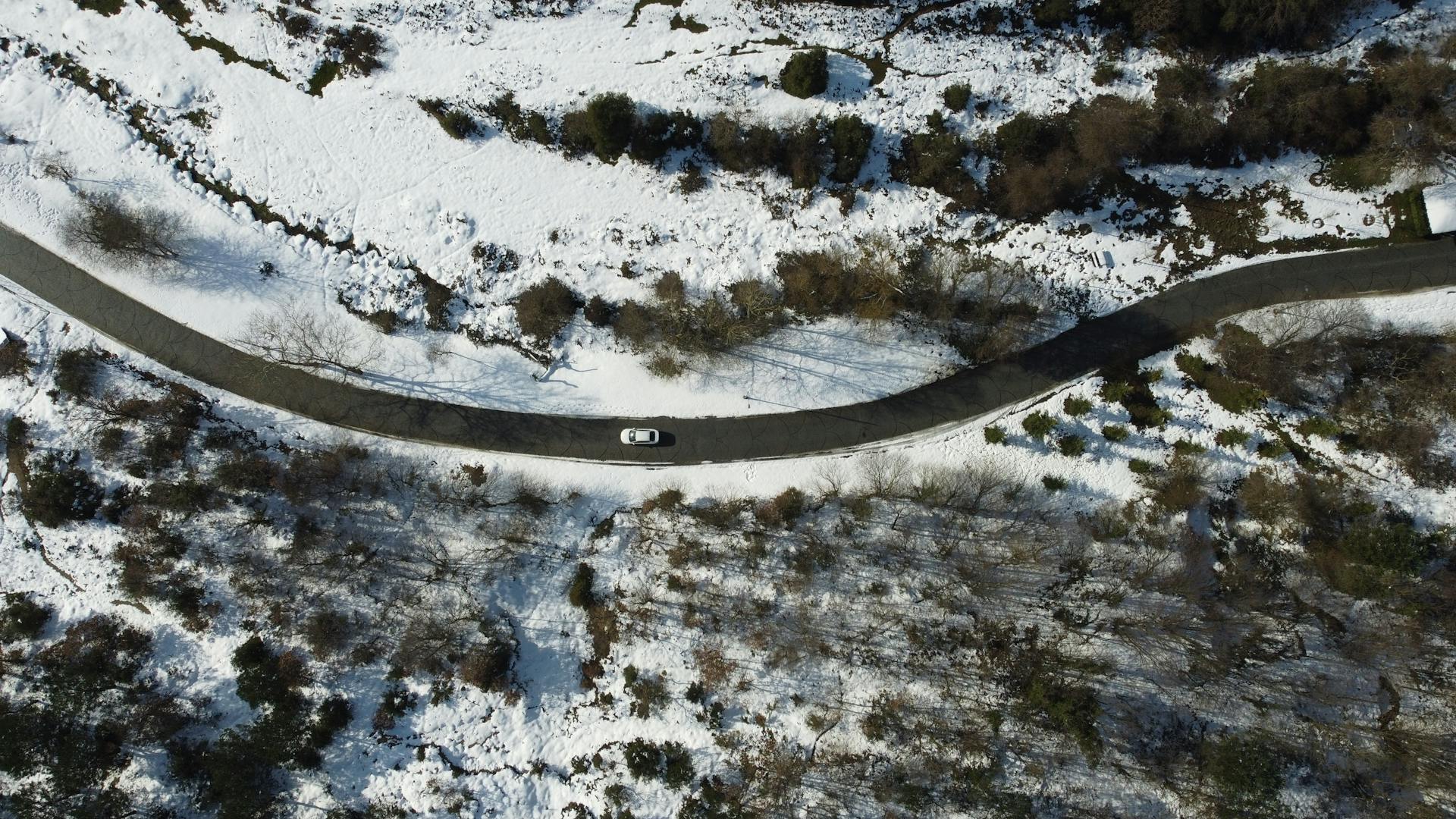 Aerial shot of a winding road through a snowy landscape and a single car.