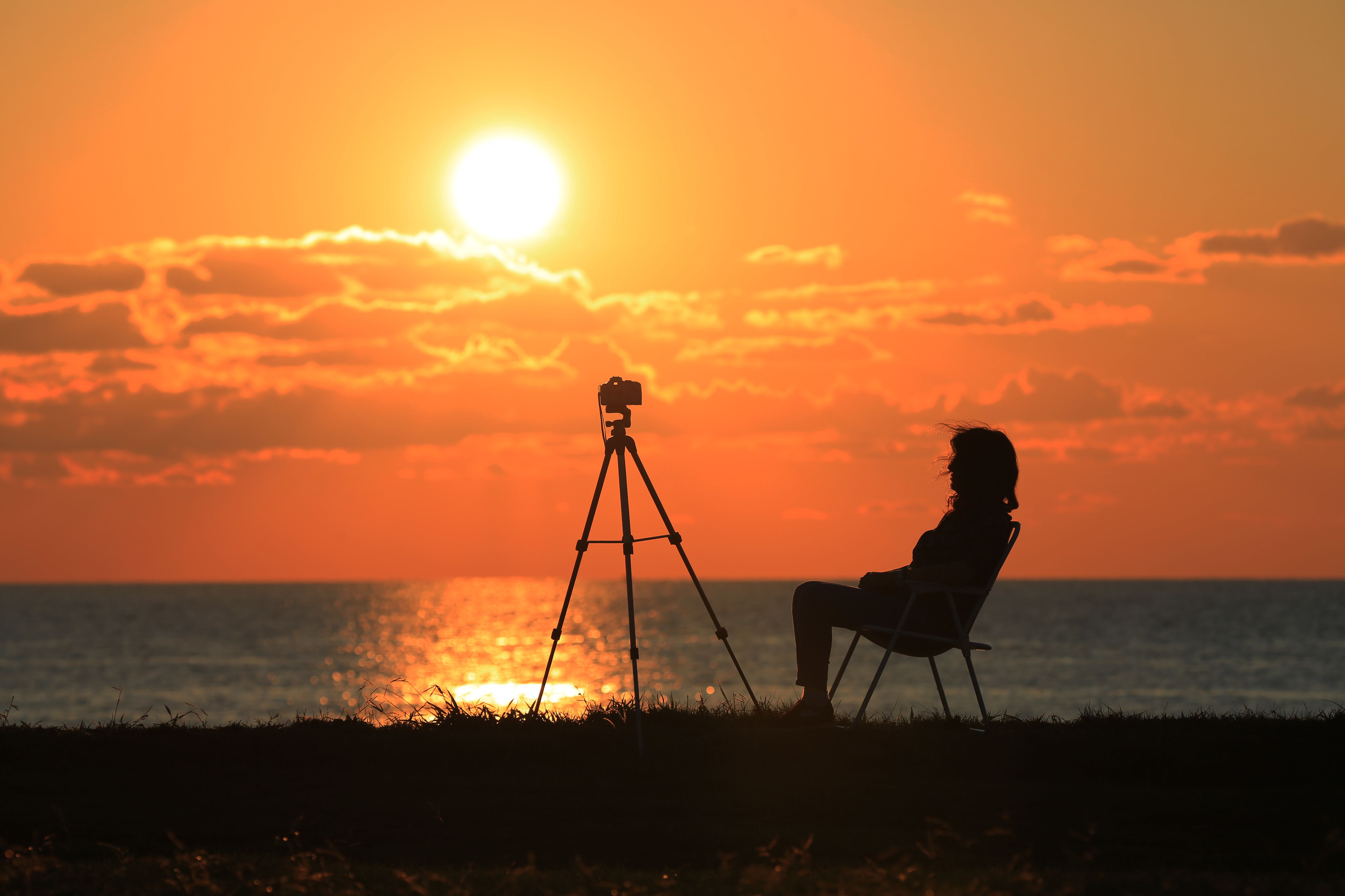 美しい海辺の夕日で撮影されたカメラと三脚を持つ女性のシルエット。